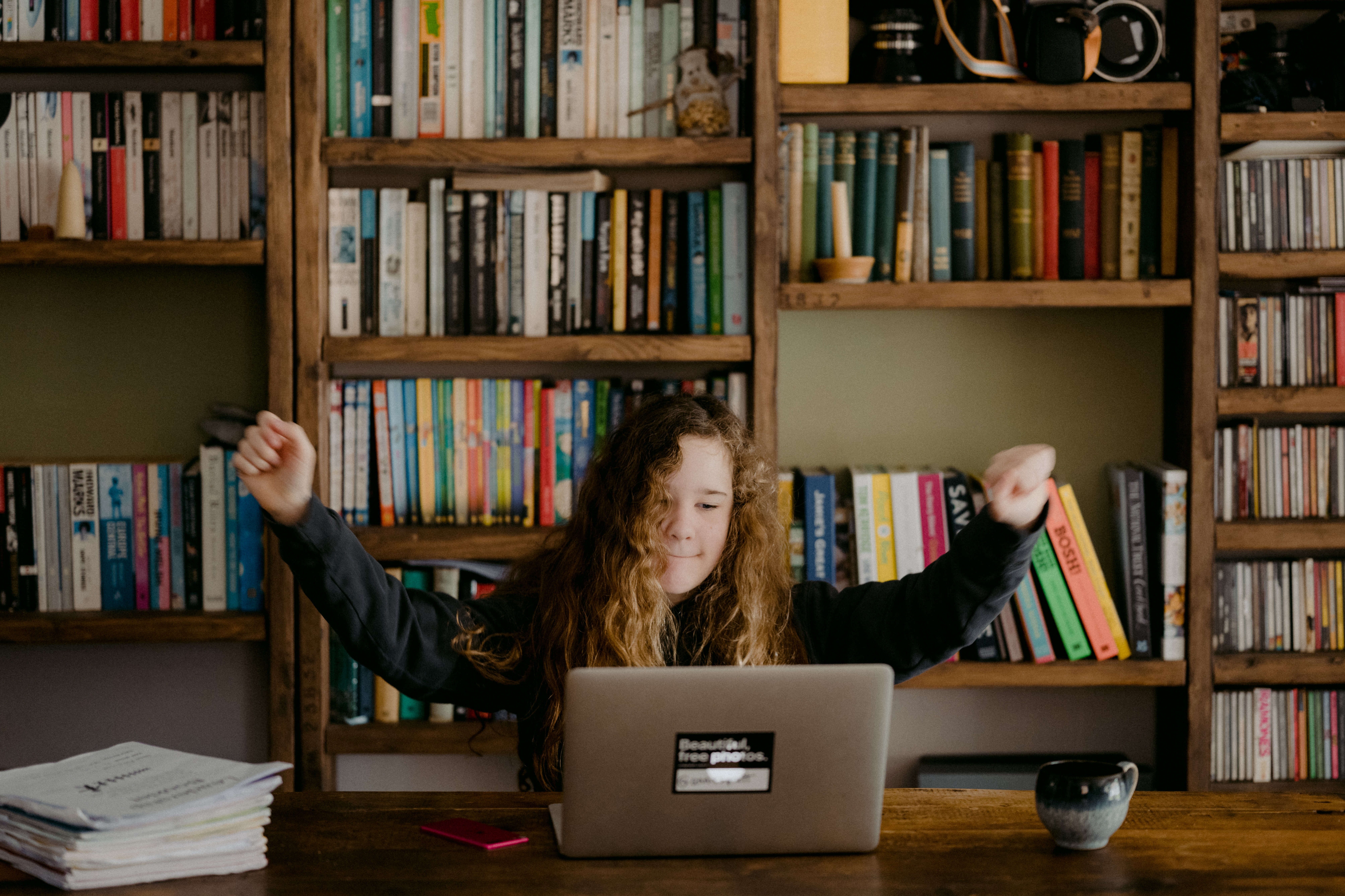 A child sitting at a computer with arms raised
