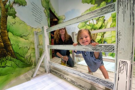 A child leaning through a fence in the Winnie the Pooh story installation