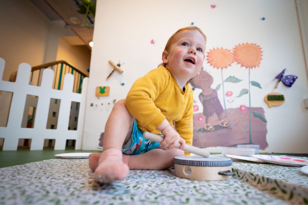 A small child banging a drum in Small Worlds