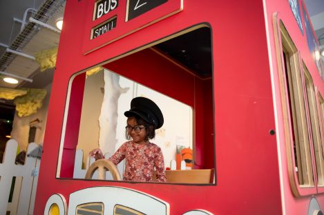 Young child pretending to drive a big red toy bus