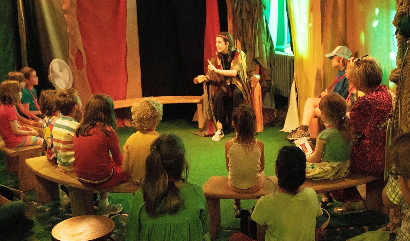 Children sat in a circle listening to a story being told.