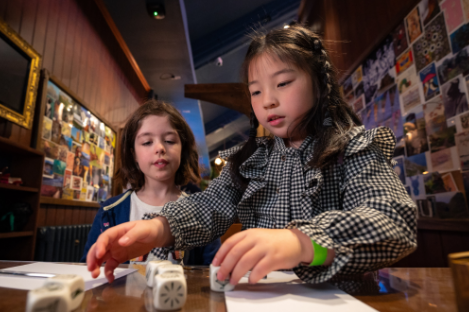 Two children sitting at C.S Lewis' desk playing with dice and writing stories.
